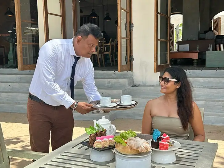 A hotel manager serves tea to a lady sitting on a table at private beach